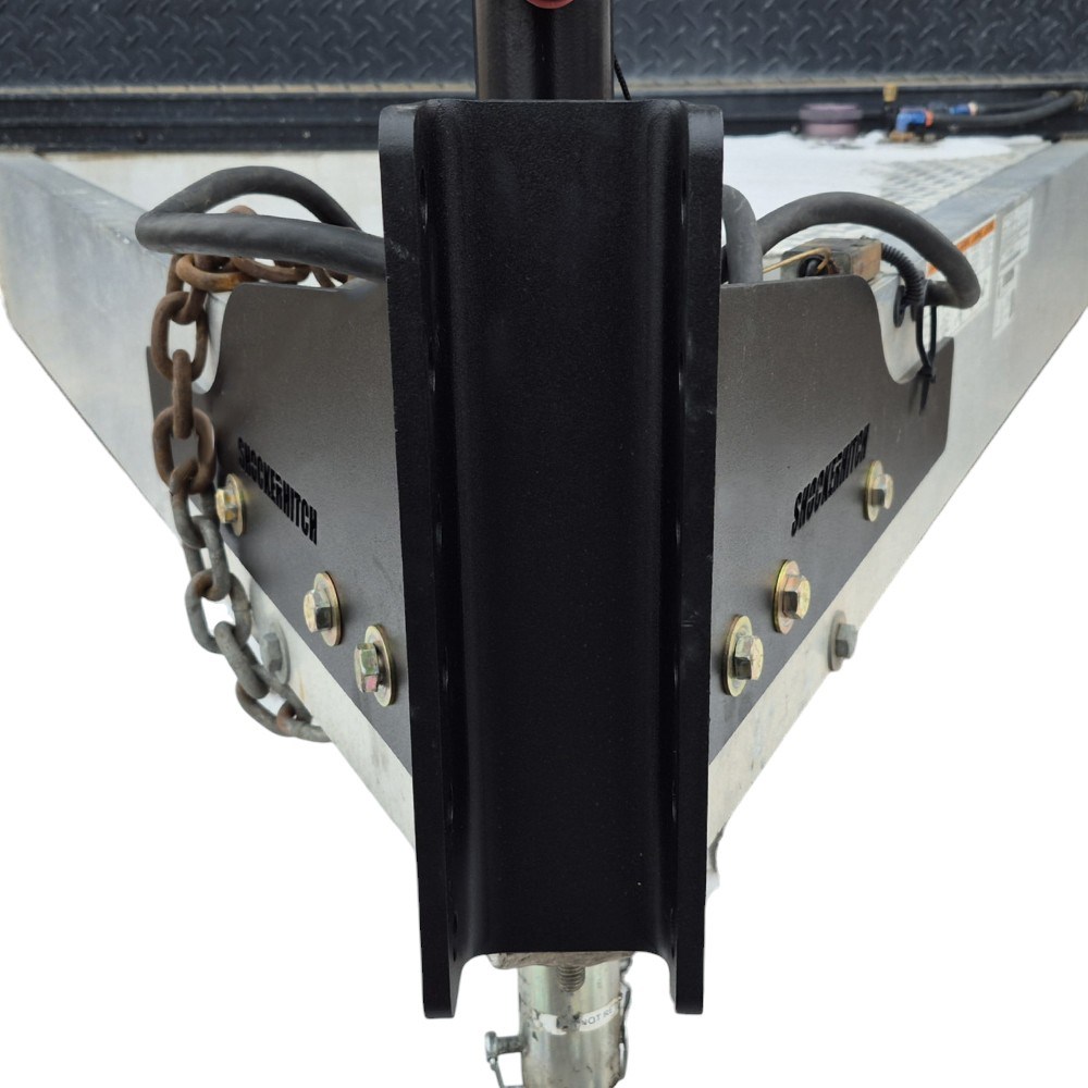 Trailer hitch coupler with safety chains mounted to a metal trailer frame.