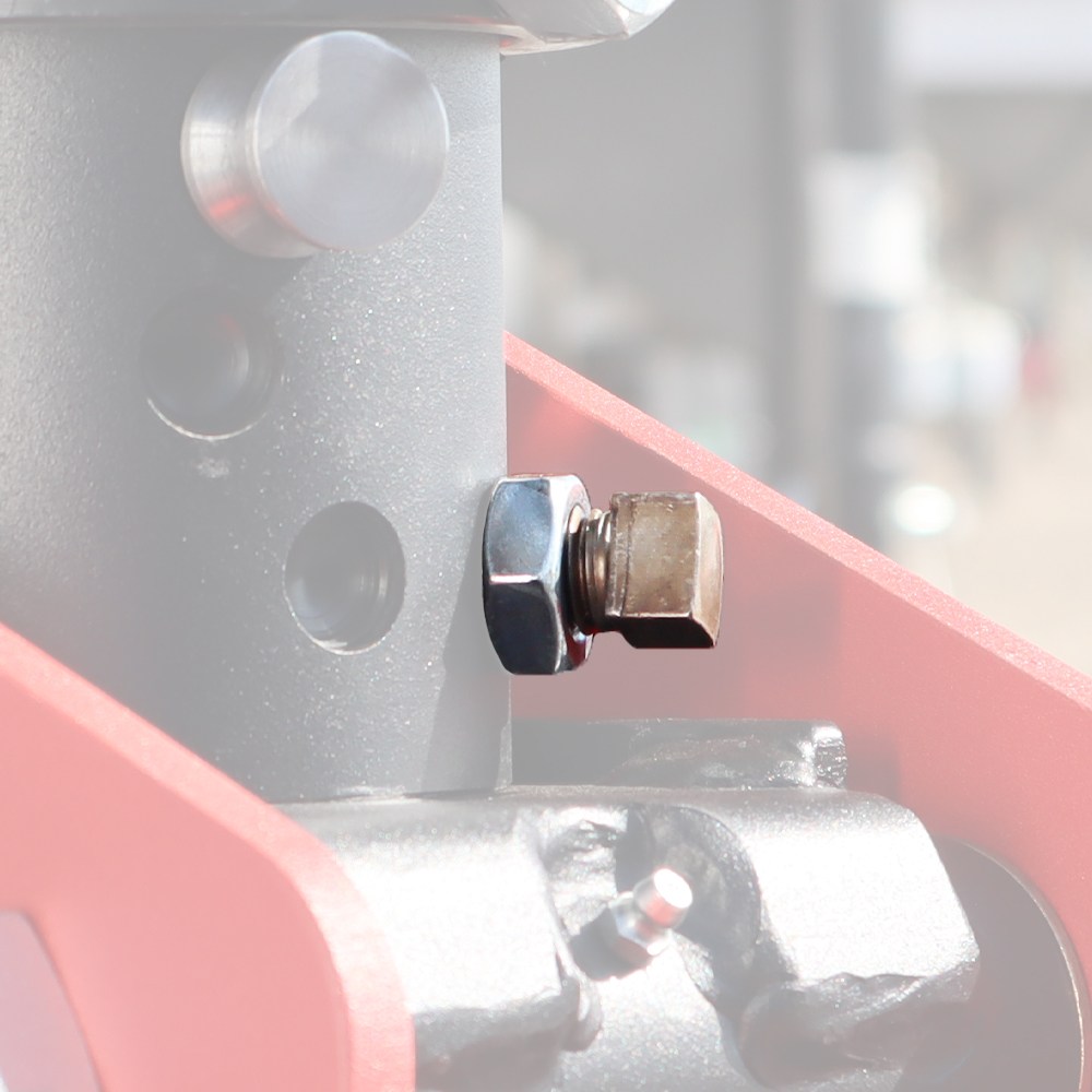 Close-up of a hex bolt and nut fastening a gray metal pillar to a red machine frame in an industrial setting.